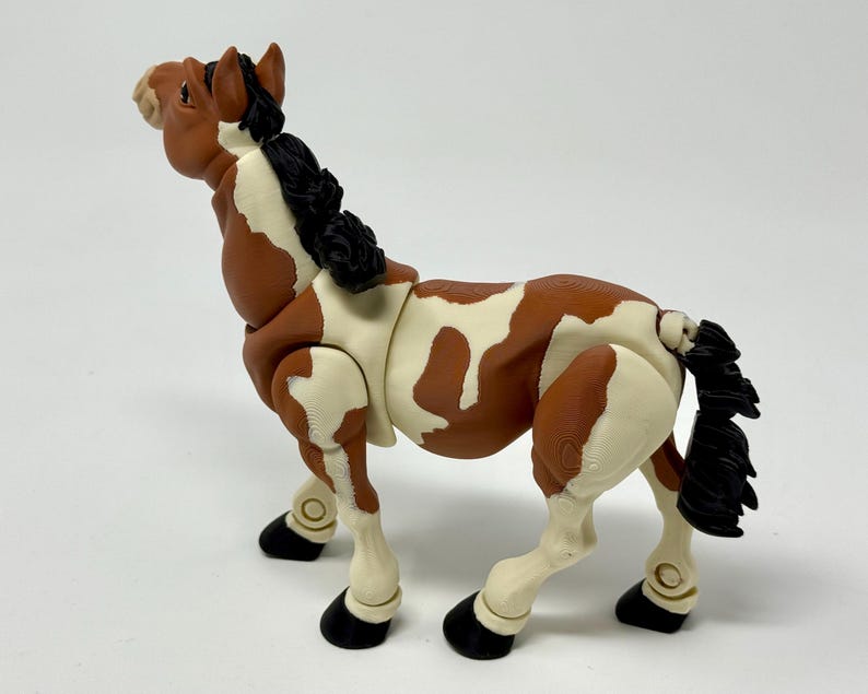 May include: A brown and white toy horse with a black mane and tail. The horse has black hooves and is posed in a standing position. The toy horse is made of plastic and has a detailed design.