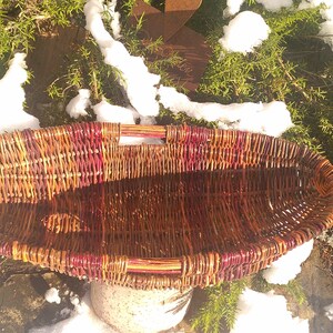 May include: A large, oval-shaped wicker basket with a reddish-brown stain. The basket has two handles and is woven with a tight, intricate pattern.