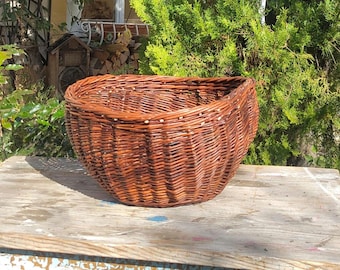 May include: A large, brown wicker basket with a rounded, oval shape. The basket is made of woven willow branches and has a natural, rustic look.