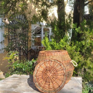 May include: A wicker basket with a lid, the lid is off and sitting on a rustic wooden table with blue paint. The basket is made of natural woven wicker.