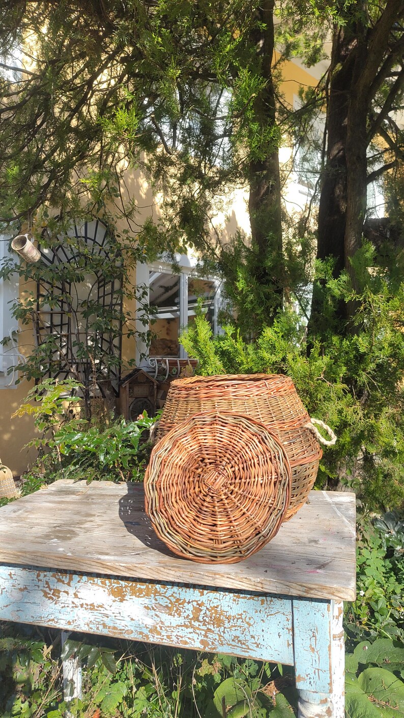 May include: A wicker basket with a lid, the lid is off and sitting on a rustic wooden table with blue paint. The basket is made of natural woven wicker.
