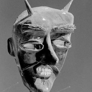 May include: A black and white image of a large, sculpted devil's head with horns. The head is made of a rough, textured material and has a fierce expression. The devil's mouth is open, revealing sharp teeth.