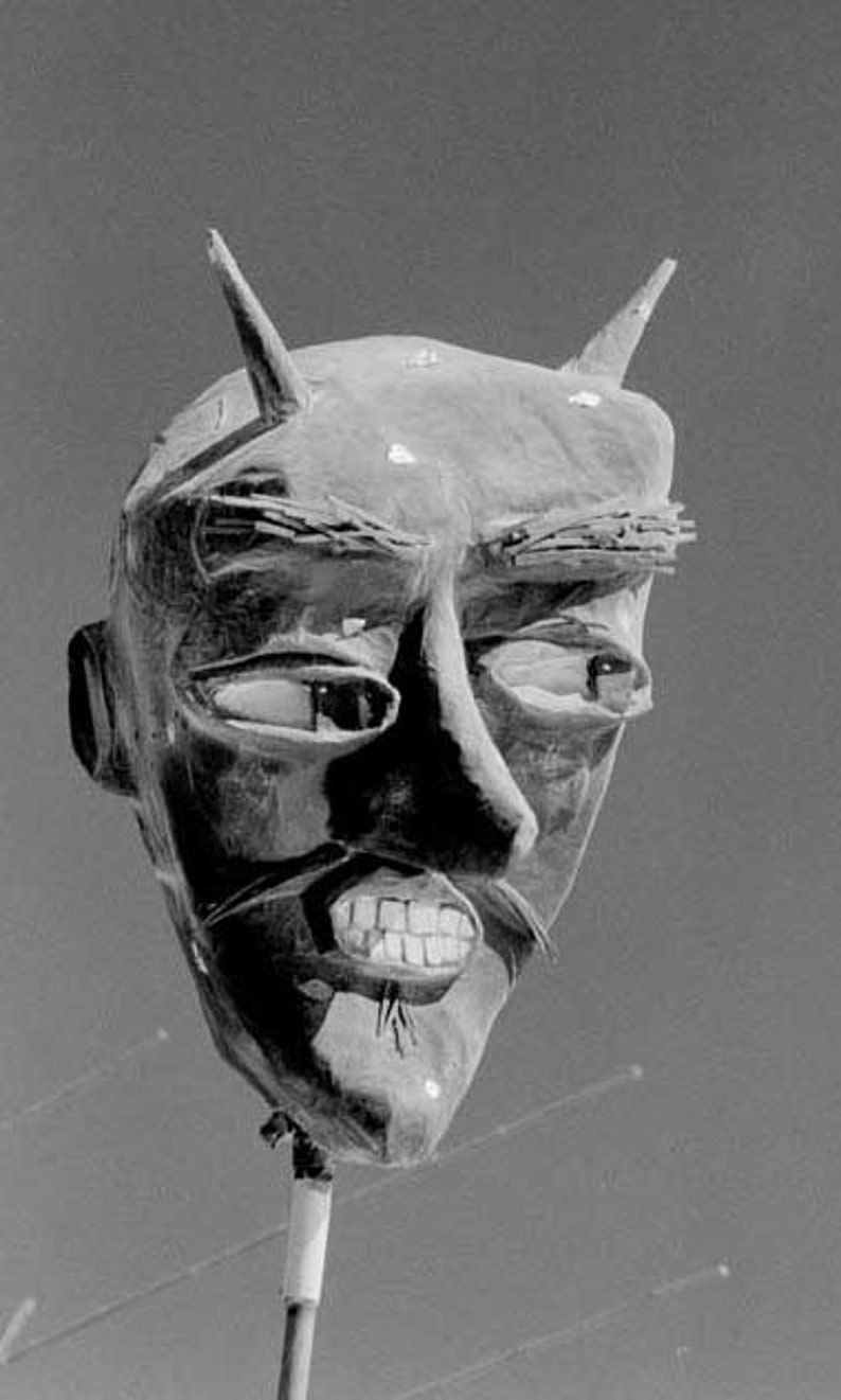 May include: A black and white image of a large, sculpted devil's head with horns. The head is made of a rough, textured material and has a fierce expression. The devil's mouth is open, revealing sharp teeth.