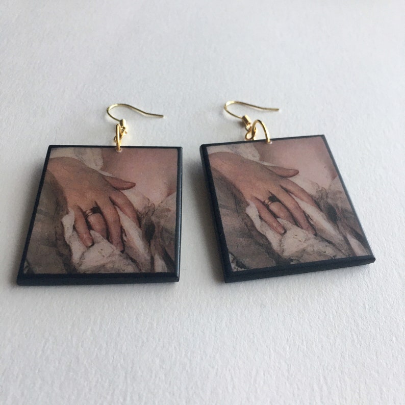 Sensual art earrings with a detail of a Romantic, Rococo lady portrait. The pose with her hand painted above her bust in the folds of her dress has an erotic connotation.