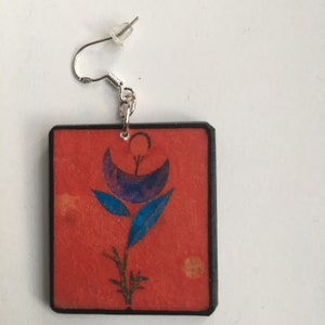 May include: Square shaped earrings with a red background and a blue and purple flower design.