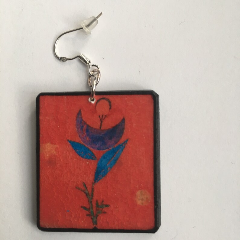 May include: Square shaped earrings with a red background and a blue and purple flower design.