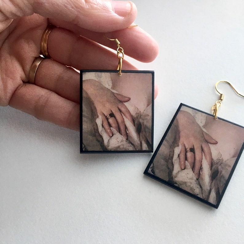Sensual art earrings with a detail of a Romantic, Rococo lady portrait. The pose with her hand painted above her bust in the folds of her dress has an erotic connotation.