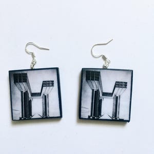 May include: A pair of square earrings featuring a black and white image of a building with columns. The earrings have silver hooks.