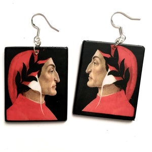May include: A pair of dangle earrings featuring a black and red portrait of a man with a laurel wreath on his head. The portrait is set in a black square frame.