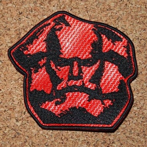 Può includere: Toppa ricamata rossa e nera con un'immagine stilizzata di un viso maschile.