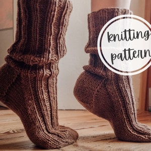May include: A pair of brown knitted socks with a ribbed pattern. The socks are folded down at the top, creating a cuff. The socks are being worn by a person, and the image is taken from a low angle. The text "knitting pattern" is superimposed on the image.