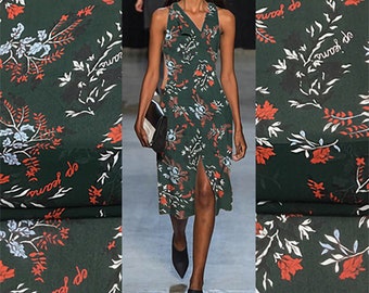 May include: A green sleeveless dress with a floral print featuring red, white, and blue flowers. The dress has a V-neckline and a slit up the front. The dress is made of a lightweight fabric and has a flowing silhouette.