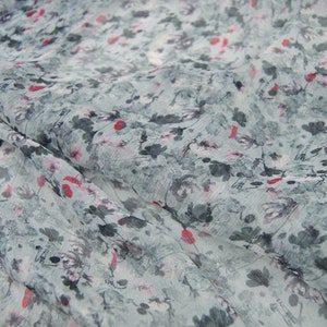 Pode incluir: Um close-up de um tecido azul claro com estampa floral. O tecido tem um brilho sutil e uma textura macia e fluida. A estampa apresenta pequenas flores delicadas em tons de rosa e vermelho, espalhadas pelo tecido.