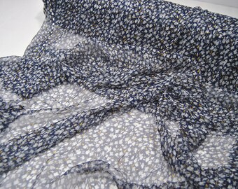 May include: A close-up of a navy blue sheer fabric with a white floral pattern. The fabric is soft and flowing, and the floral pattern is delicate and intricate.