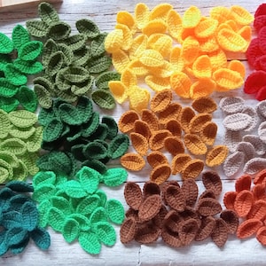 Puede incluir: Una colección de hojas de ganchillo en varios colores, incluyendo verde, amarillo, naranja, rojo, marrón y gris. Las hojas están dispuestas en grupos, mostrando las diferentes tonalidades y texturas del hilo.