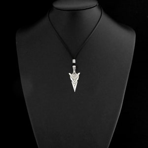 Puede incluir: Un collar con un colgante de plata con un dise&ntilde;o de punta de flecha geom&eacute;trica. El colgante est&aacute; en un cord&oacute;n negro.