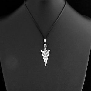 Puede incluir: Un collar de plata con un colgante de punta de flecha geom&eacute;trica. El collar est&aacute; en un expositor negro.