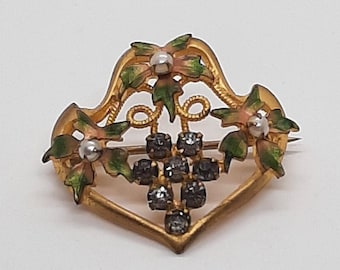 May include: A gold-toned brooch with a heart-shaped design. The brooch features a cluster of black rhinestones in the center, surrounded by green and pink enamel leaves and flowers.