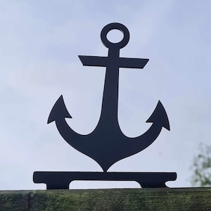 Puede incluir: Una silueta de ancla de metal negro montada sobre una superficie de madera. El ancla es un símbolo náutico popular y se utiliza a menudo como elemento decorativo.