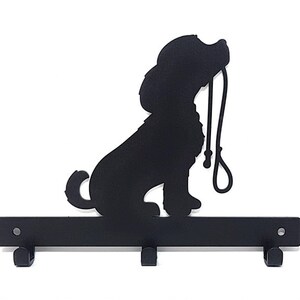 K&ouml;nnte beinhalten: Schwarzer Schl&uuml;sselhalter aus Metall in Form einer Hundesilhouette, die eine Leine h&auml;lt. Der Halter hat drei Haken zum Aufh&auml;ngen von Schl&uuml;sseln.