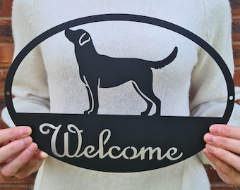 May include: Black metal oval welcome sign with a silhouette of a Labrador Retriever and the word "Welcome" in a script font.