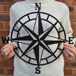 May include: Black metal compass with a star design and the letters N, S, E, and W.