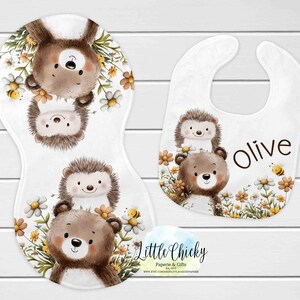 May include: A white baby burp cloth and bib set with woodland animal illustrations. The burp cloth features a bear, hedgehog, and bunny design with flowers and bees. The bib has a bear, hedgehog, and the name "Olive".