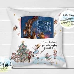 Könnte beinhalten: Ein weißes Buchkissen mit einer Tasche für ein Buch. Das Kissen zeigt eine Weihnachtsszene mit einem Baum, einem Nussknacker und Feen. Der Text "Öffne ein Buch und du kannst alles sein, was du sein möchtest" ist auf das Kissen gedruckt. Das Buch in der Tasche ist "Rudolph, das Rentier mit der roten Nase".