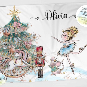 May include: Personalized Christmas-themed blanket with a ballerina, a nutcracker, a unicorn, and a mouse. The blanket is white with gold glitter and snowflakes. The text "Olivia" is written in cursive on the blanket. The blanket is 50 inches by 60 inches.
