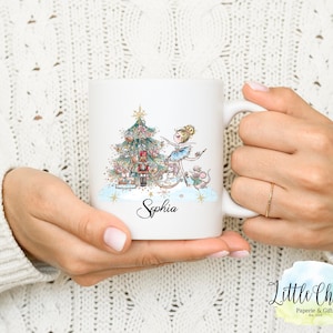 Puede incluir: Taza de cerámica blanca con un diseño navideño que incluye una bailarina, un cascanueces, un ratón y un árbol de Navidad. La taza tiene el nombre "Sophia" escrito en ella.