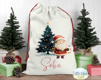 May include: A white Christmas gift bag with a red drawstring. The bag features a watercolor illustration of a Christmas tree, Santa Claus, and the name "Sofia".