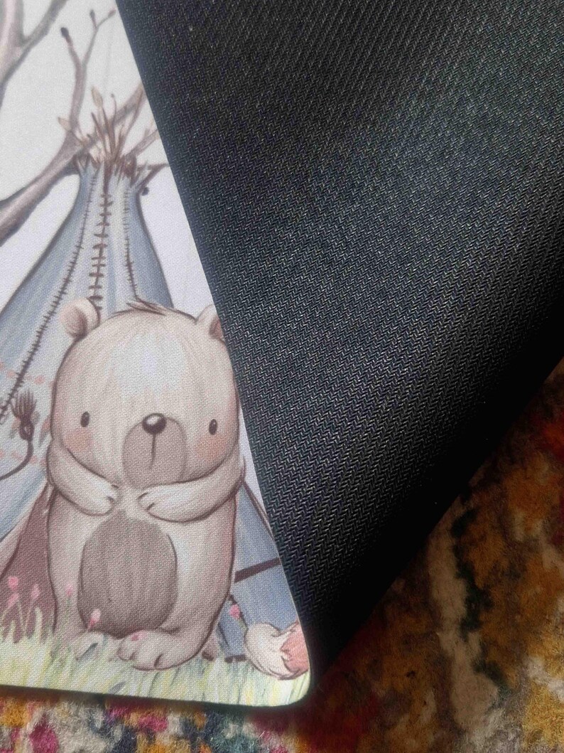 May include: A brown and white bear with a light blue teepee in the background. The bear is standing on a green patch of grass. The background is a light beige color.