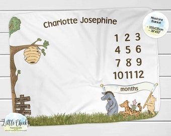 May include: A white milestone blanket with a Winnie the Pooh theme. The blanket features a beehive, a tree, and a sign that says "Welcome Hundred Aker Wood". The blanket also has a banner with the numbers 1 through 12 and the word "months". The blanket is 39 inches by 53 inches.