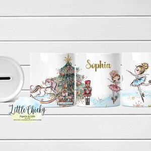 Könnte beinhalten: Weiße Keramik-Spardose mit Schlitz, mit einem Weihnachtsbaum, einem Schaukelpferd, einem Nussknacker und zwei Ballerinas. Der Name "Sophia" ist in Gold geschrieben. Die Spardose hat einen skurrilen Aquarellstil.