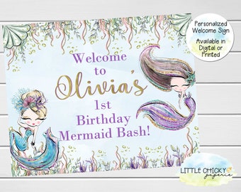May include: A welcome sign for a first birthday party with a mermaid theme. The sign is blue with purple and gold glitter accents. It says "Welcome to Olivia's 1st Birthday Mermaid Bash!" and features two cartoon mermaids.
