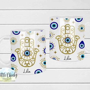 以下が含まれることがあります： 金色のハムサハンドのデザインと青い邪視が特徴の白いセラミックマグ。マグカップは青い邪視のシンボルと「Lilia」という名前で飾られています。マグカップには白いハンドルが付いています。
