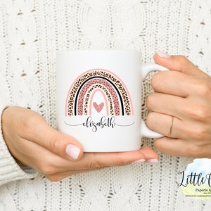 May include: White ceramic mug with a pink, black, and brown rainbow design. The rainbow has a heart in the center and the name "elizabeth" written below it.