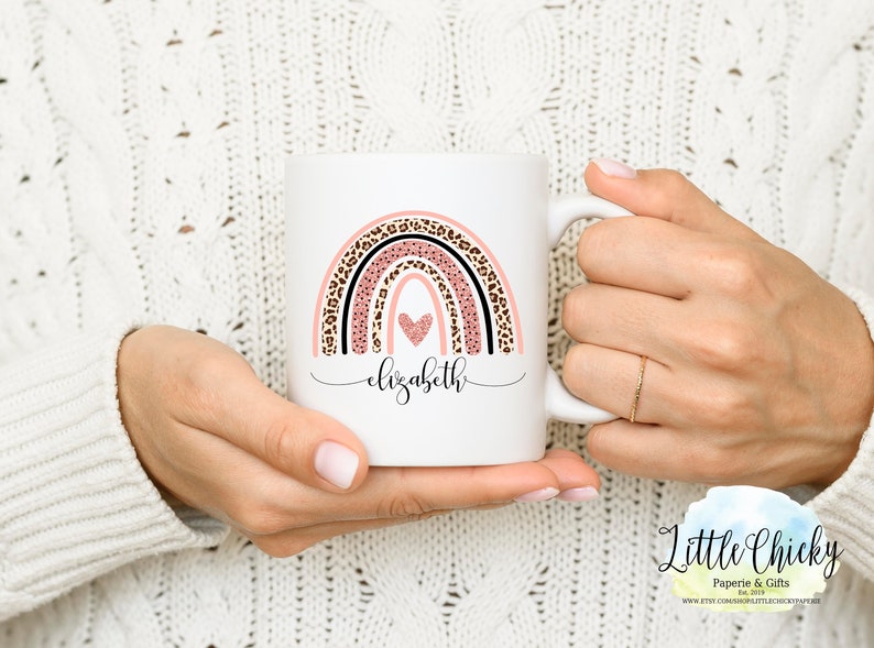 May include: White ceramic mug with a pink, black, and brown rainbow design. The rainbow has a heart in the center and the name "elizabeth" written below it.