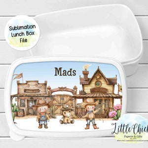 Op de afbeelding: Witte lunchbox met een sublimatieontwerp met een westerse stadsscène met twee cowboys, een beer en de naam "Mads". De lunchbox is gemaakt door Little Chickie Paperie & Gifts.