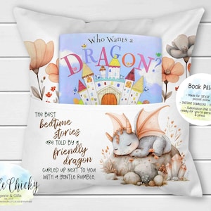 May include: White book pillow with a pocket, featuring a children's book titled "Who Wants a Dragon?" and a watercolour illustration of a sleeping dragon. The pillow has floral accents and text that reads "The Best bedtime stories are told by a friendly dragon."