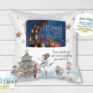 Könnte beinhalten: Weißes Buchkissen mit einer Tasche, die ein Buch mit dem Titel "Rudolph the Red-Nosed Reindeer" enthält. Das Kissen zeigt einen Weihnachtsbaum, Ballerina-Illustrationen und den Text "Open a book and you can be anything you want to be."