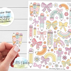以下が含まれることがあります： パステルカラーの鉛筆とリボンのデザインのステッカーシート。ステッカーには「Sticker Sheet A6 Sheets 10.4cm x 14.7cm」と「Coquette Pencils」の文字が含まれています。ステッカーは手で持たれています。