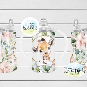 May include: A 12 ounce clear plastic sippy cup with a floral and giraffe design. The cup has two handles and a straw lid. The cup is personalized with the name "Lilia" and the text "Little Chickie Paperie & Gifts".