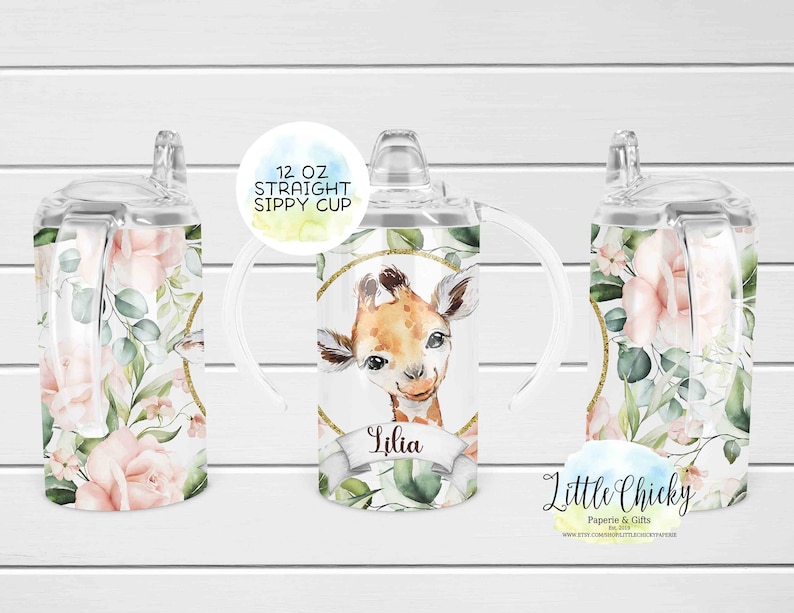 May include: A 12 ounce clear plastic sippy cup with a floral and giraffe design. The cup has two handles and a straw lid. The cup is personalized with the name "Lilia" and the text "Little Chickie Paperie & Gifts".