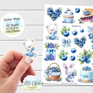 Può includere: Un foglio di adesivi con illustrazioni a tema mirtilli. I disegni includono un orsacchiotto, un coniglietto, un cupcake, una torta e forme di cuore, tutti adornati con mirtilli. Il foglio include anche il testo "Sticker Sheet" e dimensioni di 148x105mm.