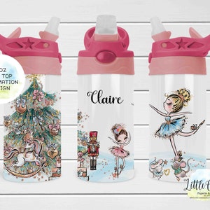 Puede incluir: Una botella de agua rosa de 350 ml con tapa abatible y un diseño de sublimación que presenta un árbol de Navidad, un unicornio, una bailarina y un cascanueces. La botella tiene el nombre "Claire" escrito en ella.