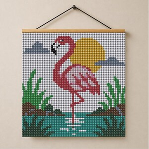 May include: A square diamond painting wall hanging featuring a pink flamingo standing in teal water. The scene includes a yellow sun, grey clouds, and green foliage. The artwork is constructed from small, circular, faceted beads on a grid.