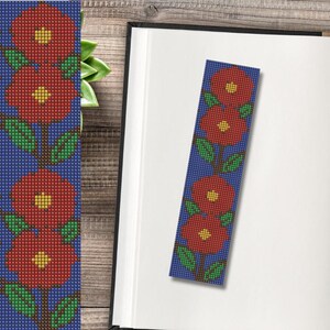 Op de afbeelding: Een blauwe boekenlegger met een bloemenontwerp. De boekenlegger heeft drie rode bloemen met gele centra en groene bladeren, verticaal gerangschikt op een blauwe achtergrond. Het ontwerp doet denken aan kruissteek.