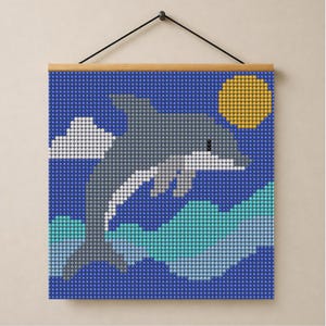 May include: A square diamond painting wall hanging featuring a grey dolphin leaping over stylised teal and light blue waves against a dark blue background with a white cloud and a yellow sun, suspended from a wooden rod with a black cord.