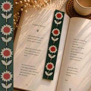 May include: A green bookmark with a floral pattern featuring red and white flowers. The bookmark is placed in an open book with the title "A Quiet Place" visible. The book's pages display printed text.